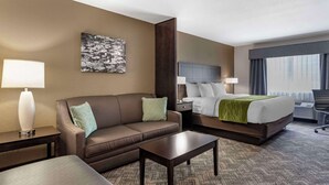 A hotel room with a sofa, a bed, a coffee table, and a painting on the wall.