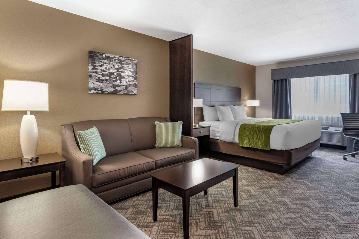 Una habitación de hotel con sofá, cama, una mesita de centro y un cuadro en la pared.