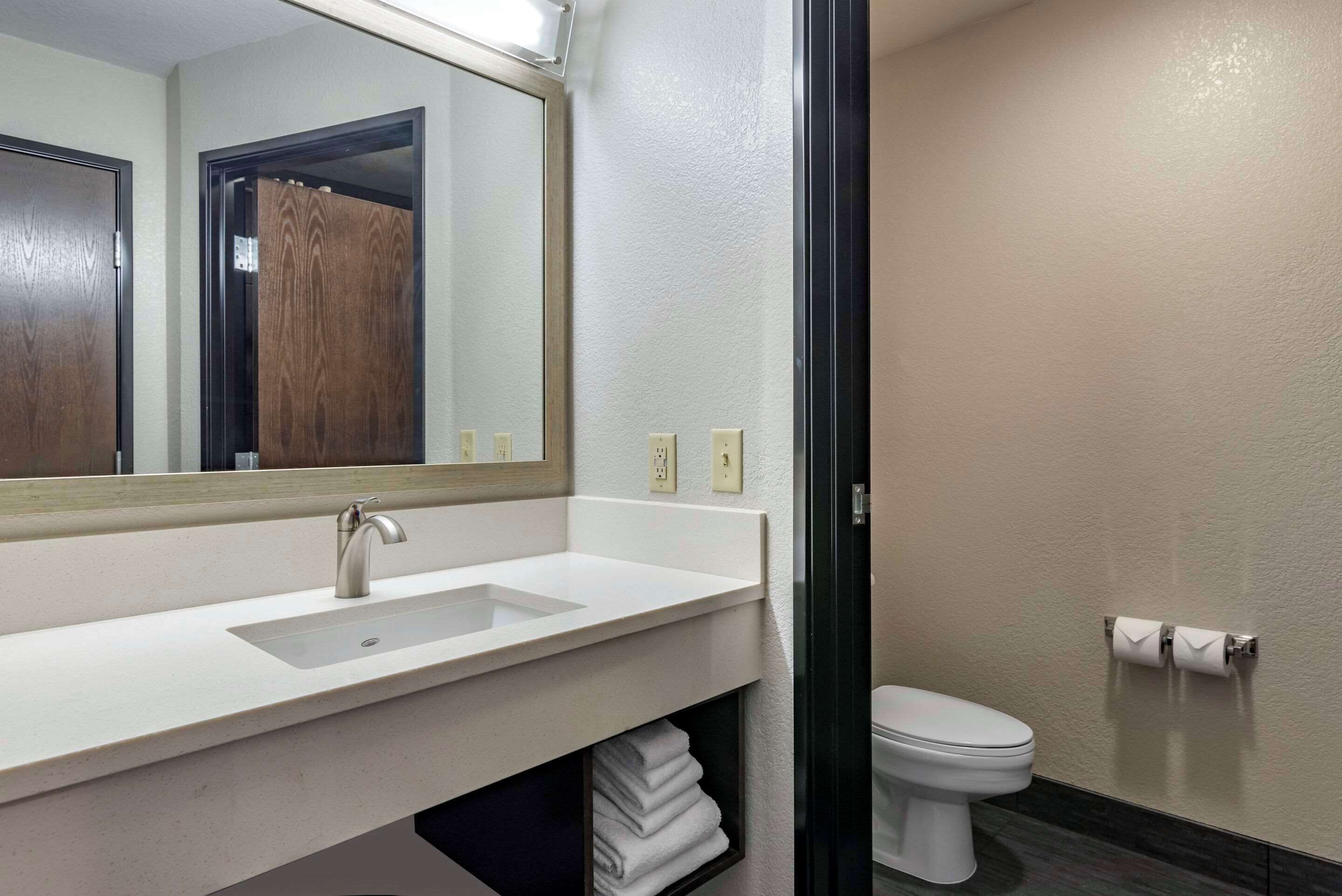 A modern bathroom with a white sink, a mirror, a toilet, and a towel rack.