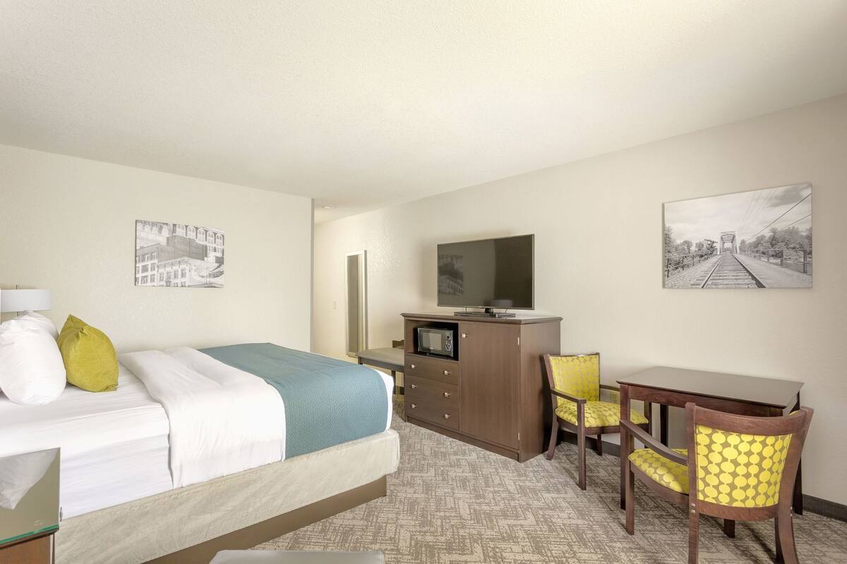 Une chambre d’hôtel équipée d’un lit, d’un bureau, d’une chaise, d’une télévision et de deux tableaux accrochés au mur.