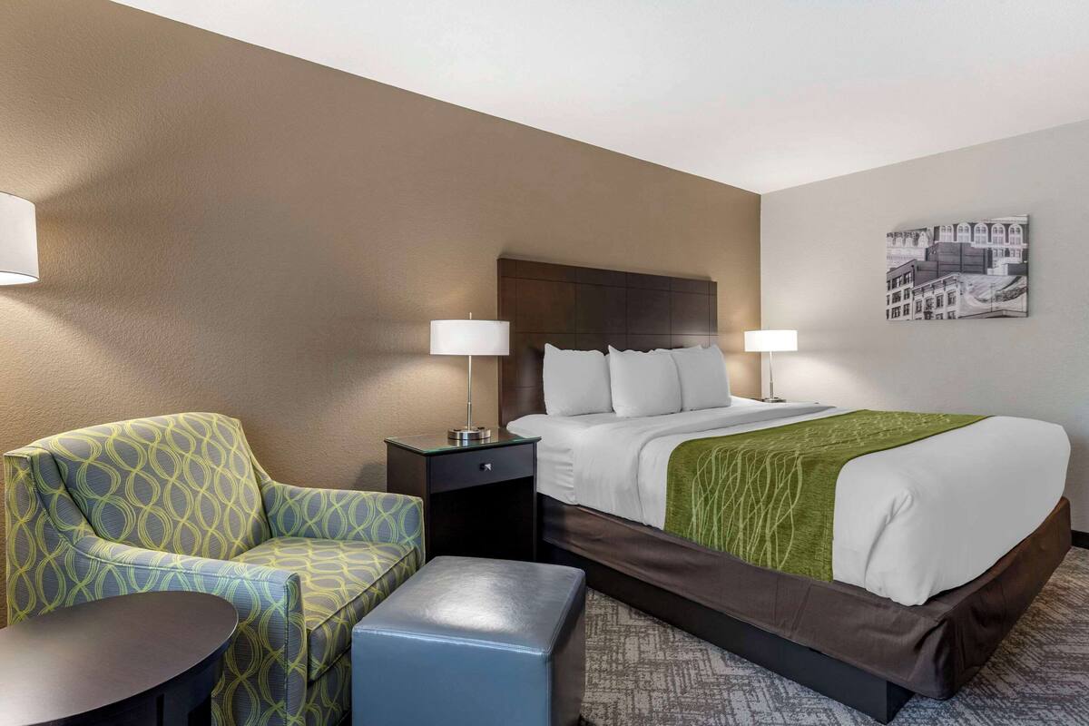 Una habitación de hotel con una cama, dos mesitas de noche, una silla y una pequeña mesa.