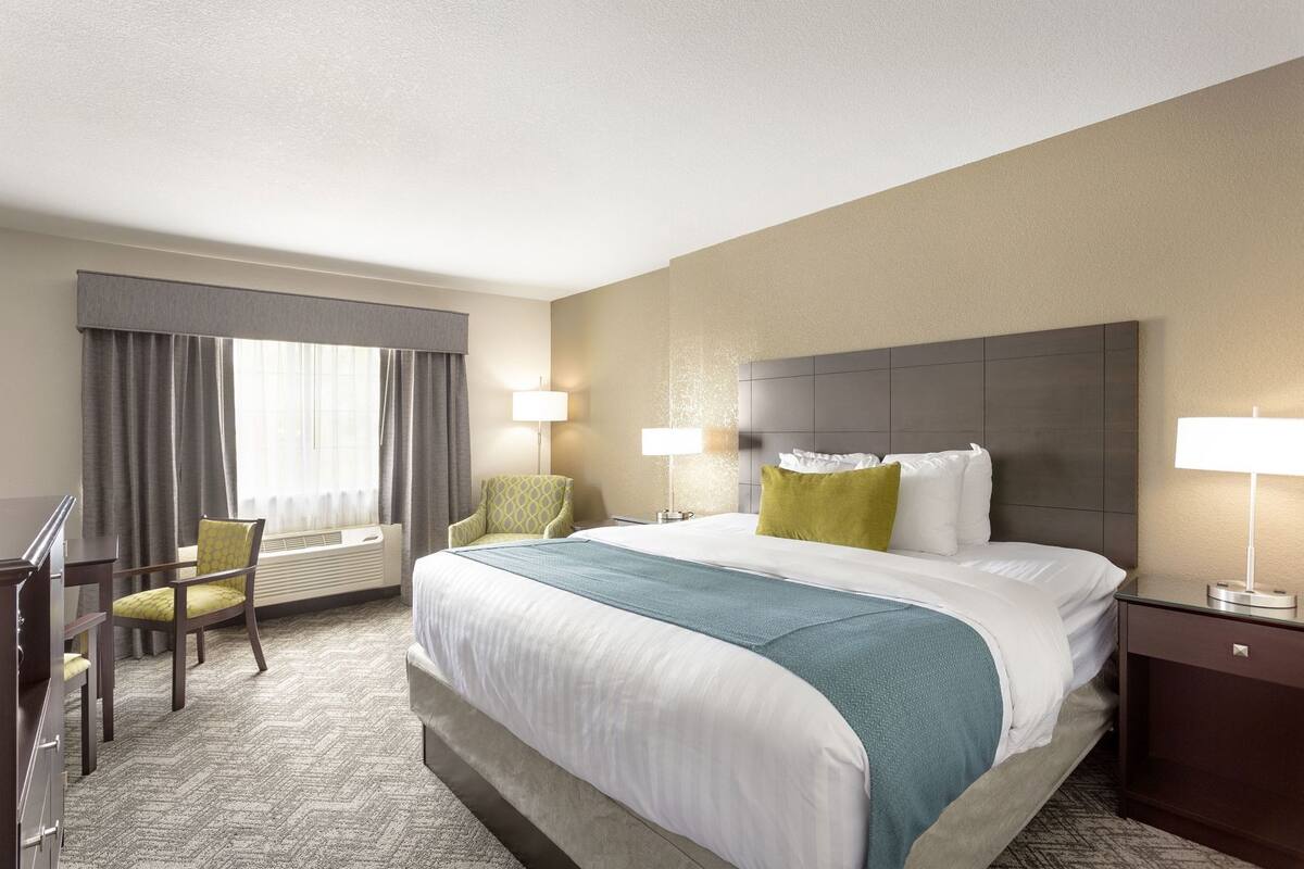 Una habitación de hotel con una cama grande, dos sillas, un escritorio y una lámpara.