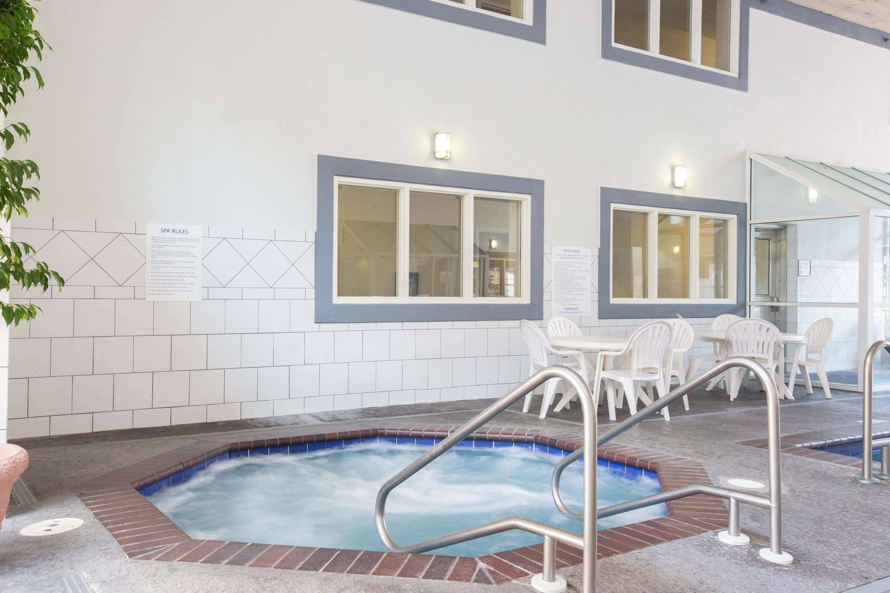 A pool area with a hot tub, seating, and spa rules sign.