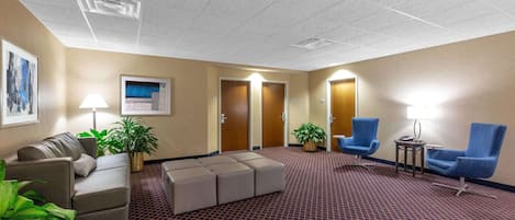 A hotel lobby with a patterned carpet, seating area with chairs, a sofa, and a small table with a lamp.