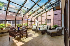A sunroom with a glass ceiling, wicker furniture, and potted plants. - Baymont by Wyndham Des Moines Airport (Des Moines)