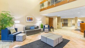 Un vestíbulo amplio con techo alto, zona de estar con sofás y otomanas, mostrador de recepción y una escalera a un nivel superior.