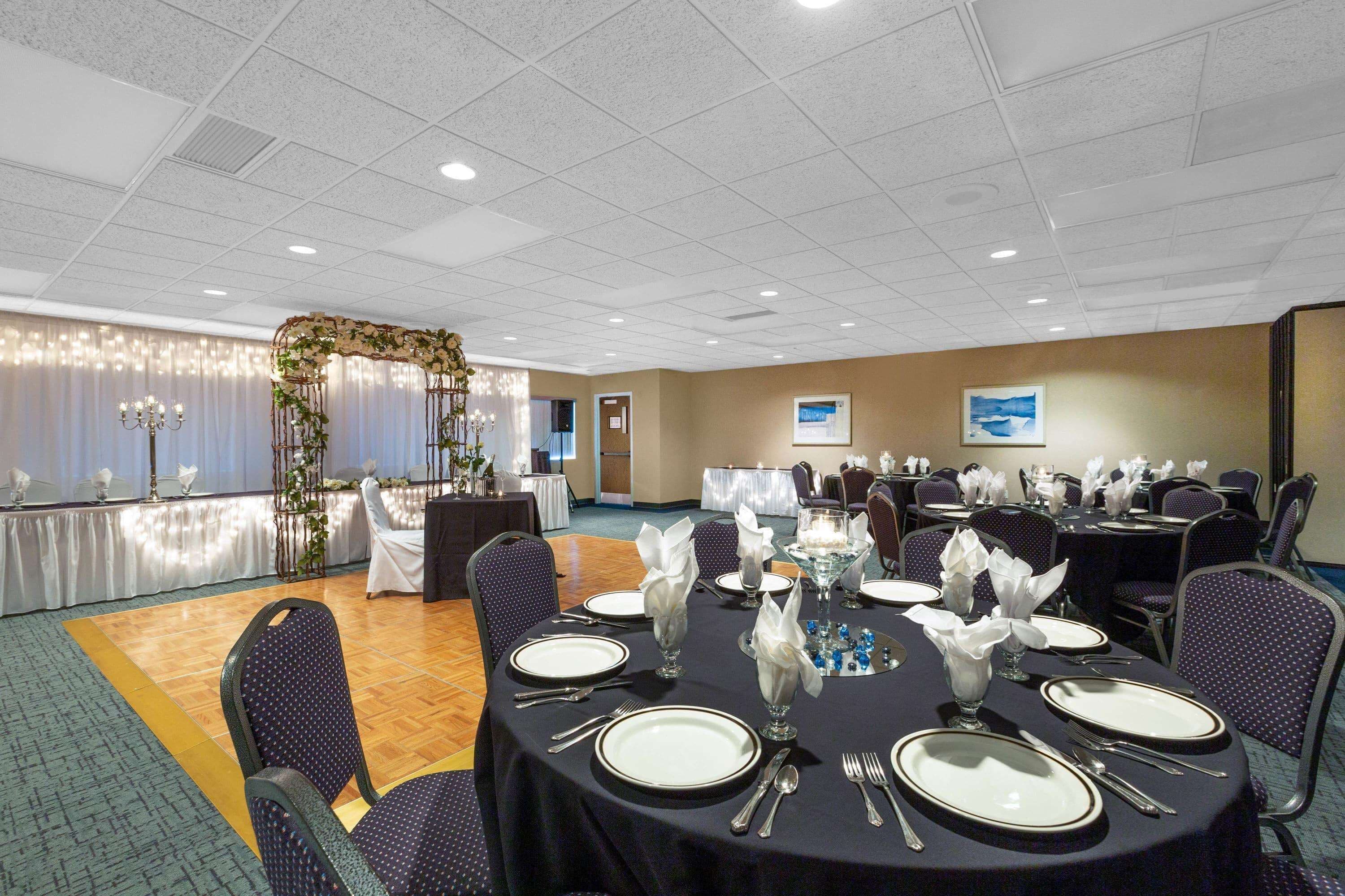 Une salle de banquet avec des tables rondes dressées pour le repas, des chaises et une composition florale décorative.