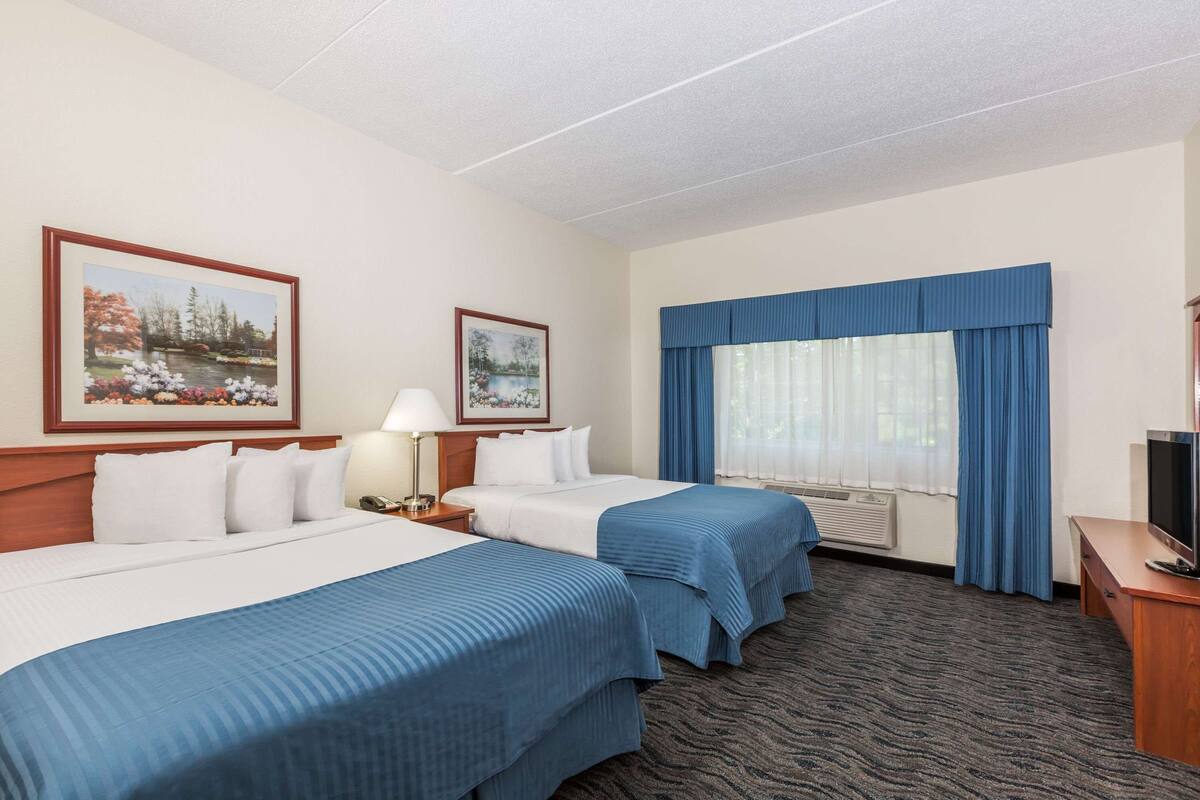 A hotel room with two beds, a TV, a desk, and a window with curtains.