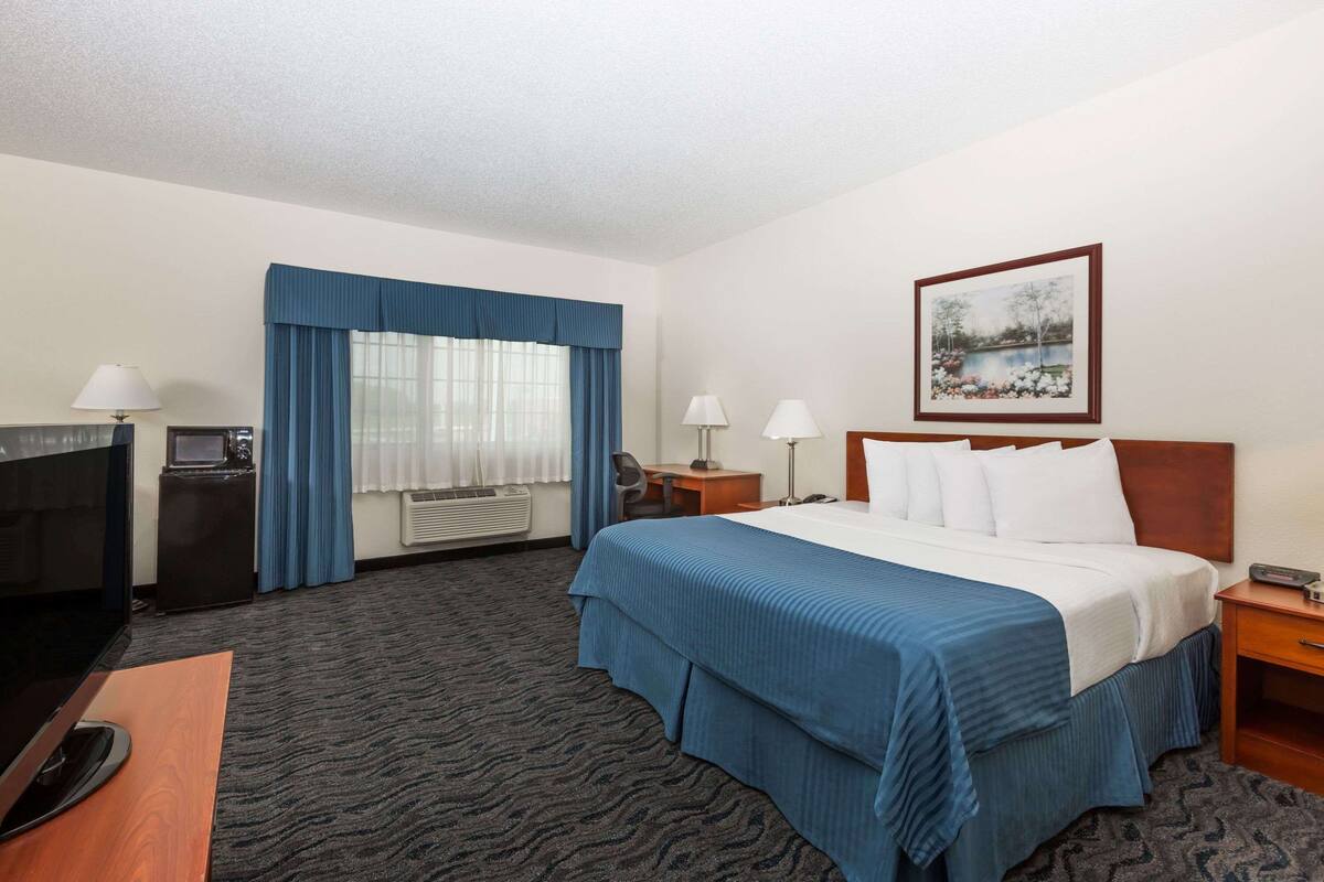 A hotel room with a bed, two bedside tables, a desk with a lamp, a television, and a window with curtains.