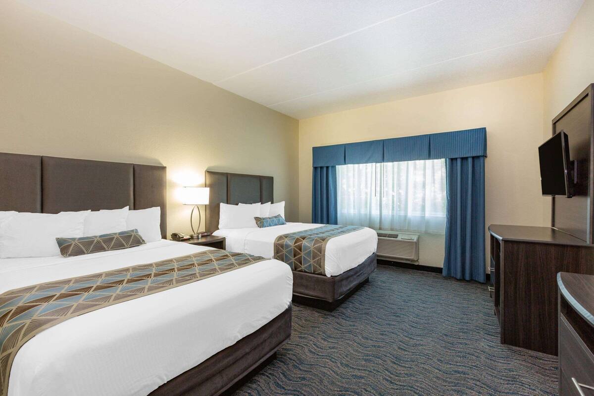 A hotel room with two beds, a desk, a TV, and a window with curtains.