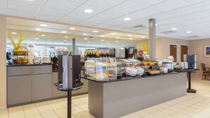Un área de desayuno limpia y bien iluminada con autoservicio, una máquina de café y una variedad de alimentos.