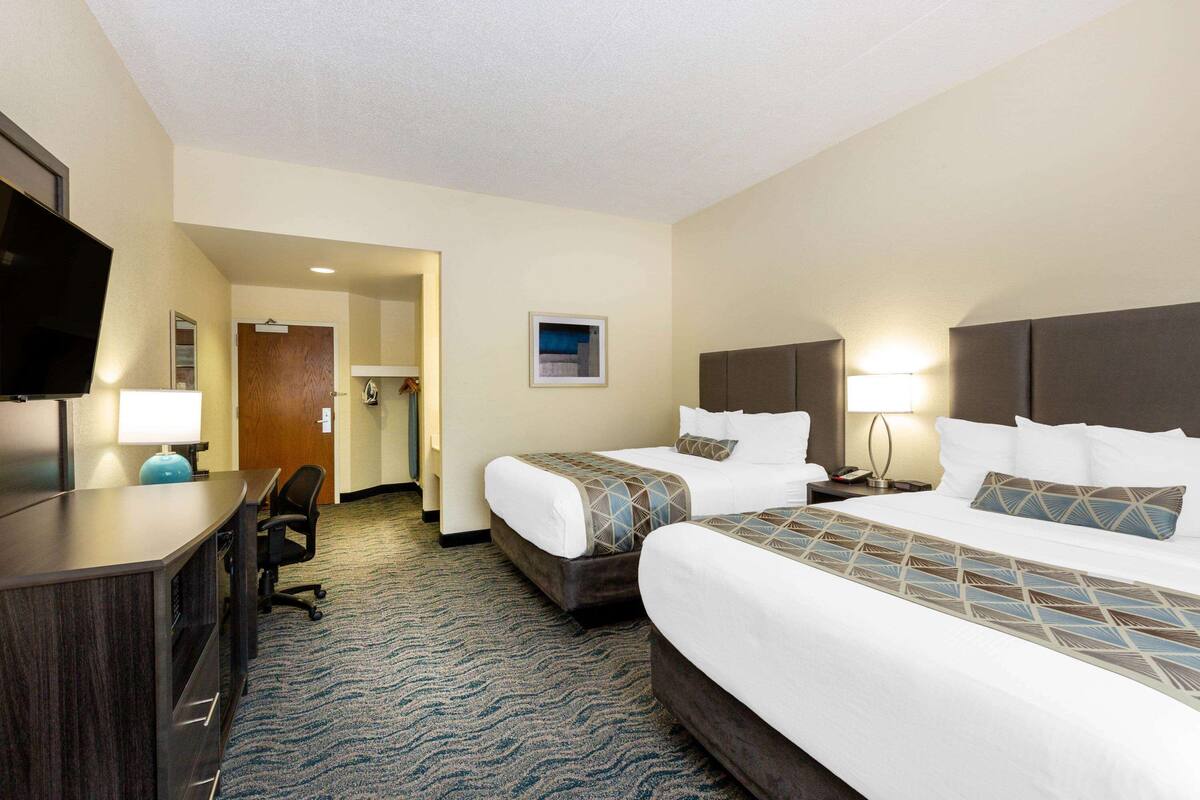 A hotel room with two beds, a desk, a chair, a TV, and a door leading to a bathroom.