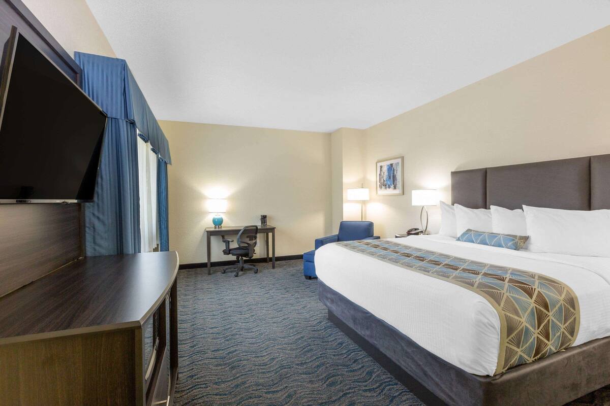A hotel room with a bed, a desk, a chair, a television, and a lamp.