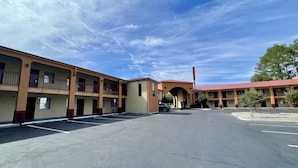 A multi-story motel with a central courtyard, outdoor parking, and a clear sky.