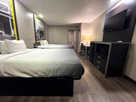 Habitación de hotel con dos camas, un escritorio, una silla, un televisor y un armario.