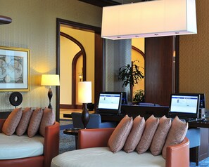 A hotel lobby with two seating areas, each with a laptop, a lamp, and a framed map on the wall.