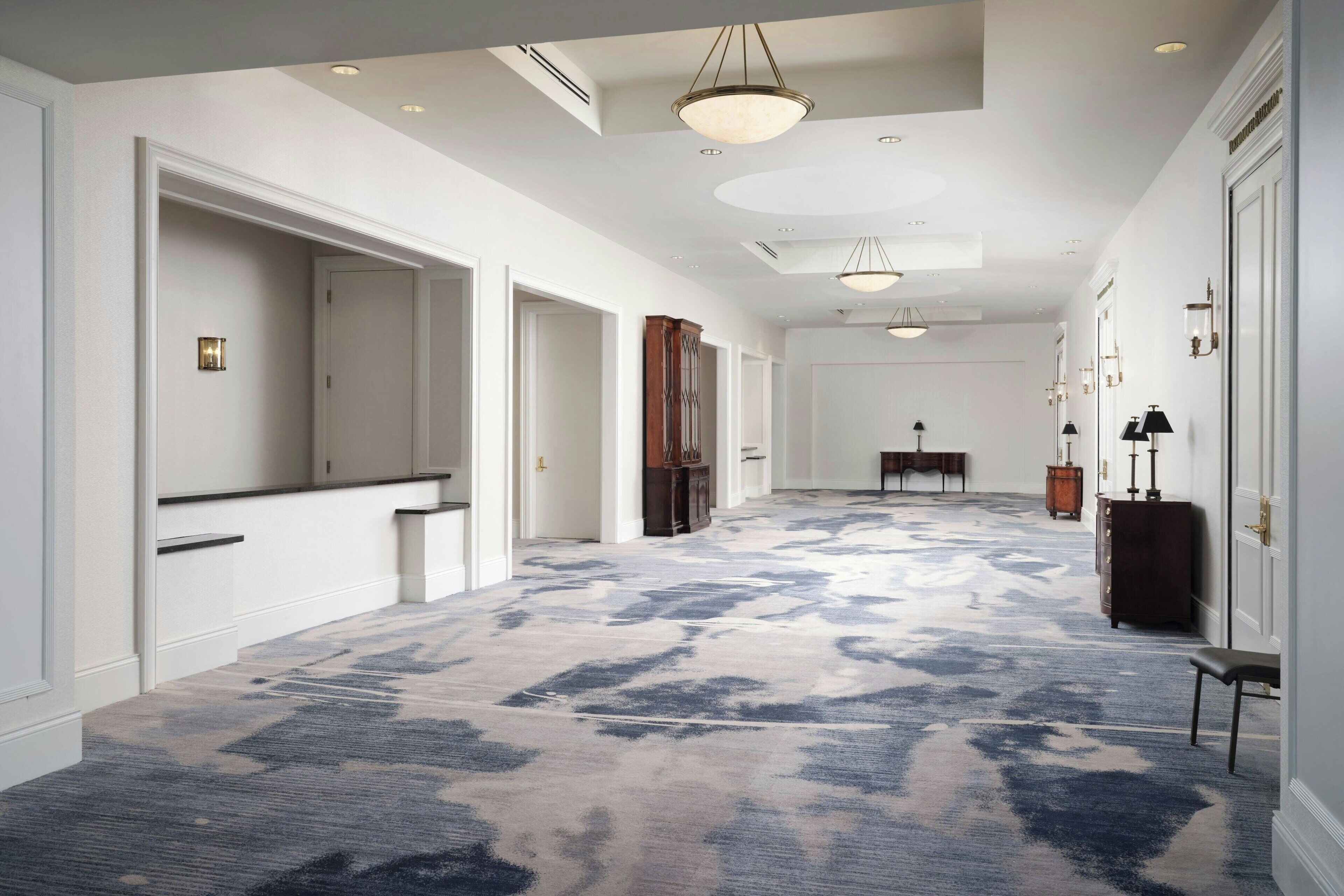 A spacious hallway with a patterned carpet, a grand piano, and a large mirror on the left.