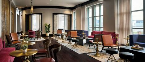A spacious hotel lobby with a central seating area, multiple tables, and large windows providing views.
