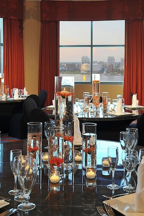 A dining table set for a meal with candles, glasses, and a view of the cityscape through large windows.