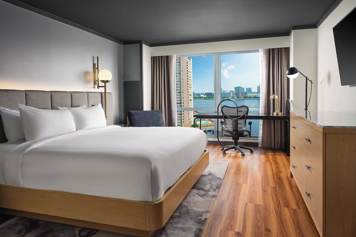 Une chambre d’hôtel moderne dotée d’un grand lit, d’un bureau avec une chaise, d’une vue sur la ville et d’une grande fenêtre.