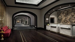 Eine Hotelhalle mit einer langen Korridor, einer roten Sitzgelegenheit, einem мраморнем Empfangsschalter und einer Decke mit Dachfenster.