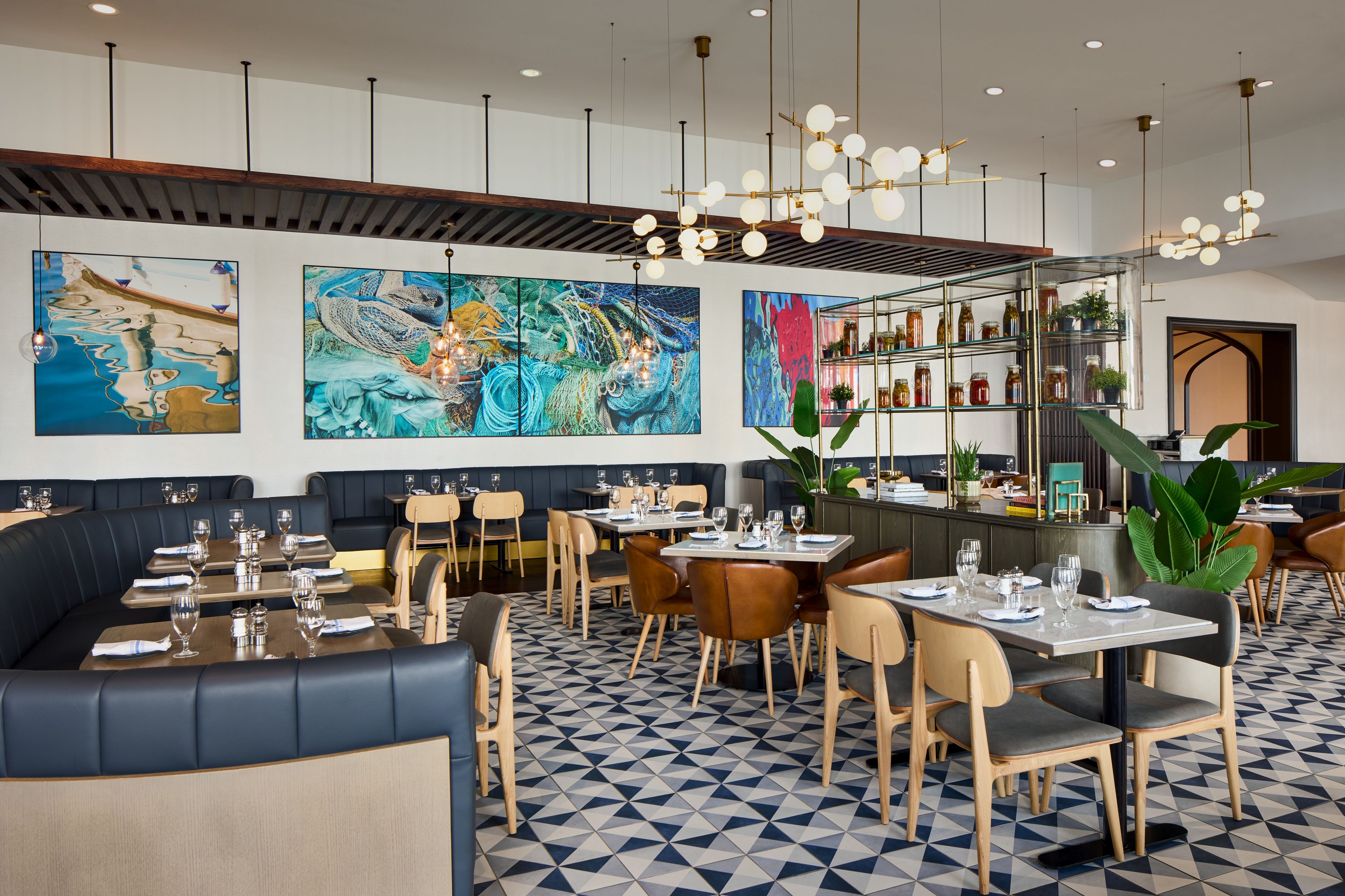 A restaurant with a modern interior, featuring a mix of seating options including booths and tables, a patterned floor, and large abstract wall art.