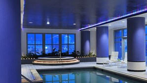 Ein moderner Innenpool mit Blick auf die Stadt, großen Fenstern und einer Sitzecke mit Liege am Pool.