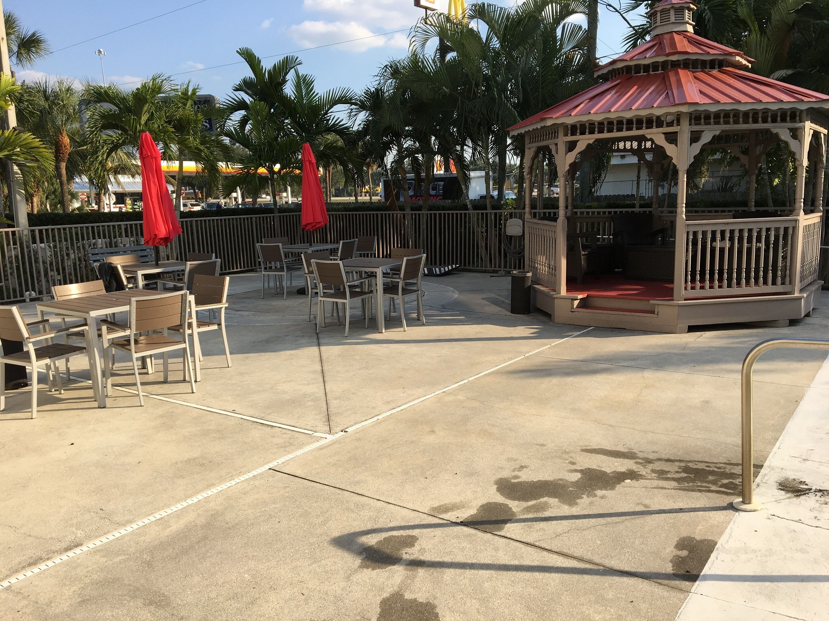 An outdoor seating area with tables and chairs, a gazebo, and palm trees.