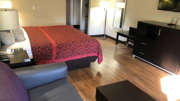 A hotel room with a bed, a desk, a dresser, a TV, and a lamp.