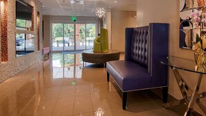 Een hal met een blauwe gestoffeerde fauteuil, een groene accentstoel en een glazen tafel.
