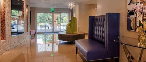 A lobby with a blue upholstered chair, a green accent chair, and a glass table.
