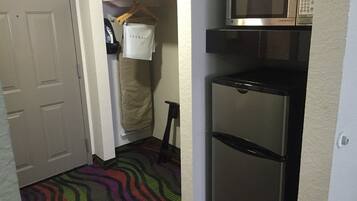 Una cocina compacta con microondas y refrigerador, una alfombra colorida y un armario con ropa colgada.