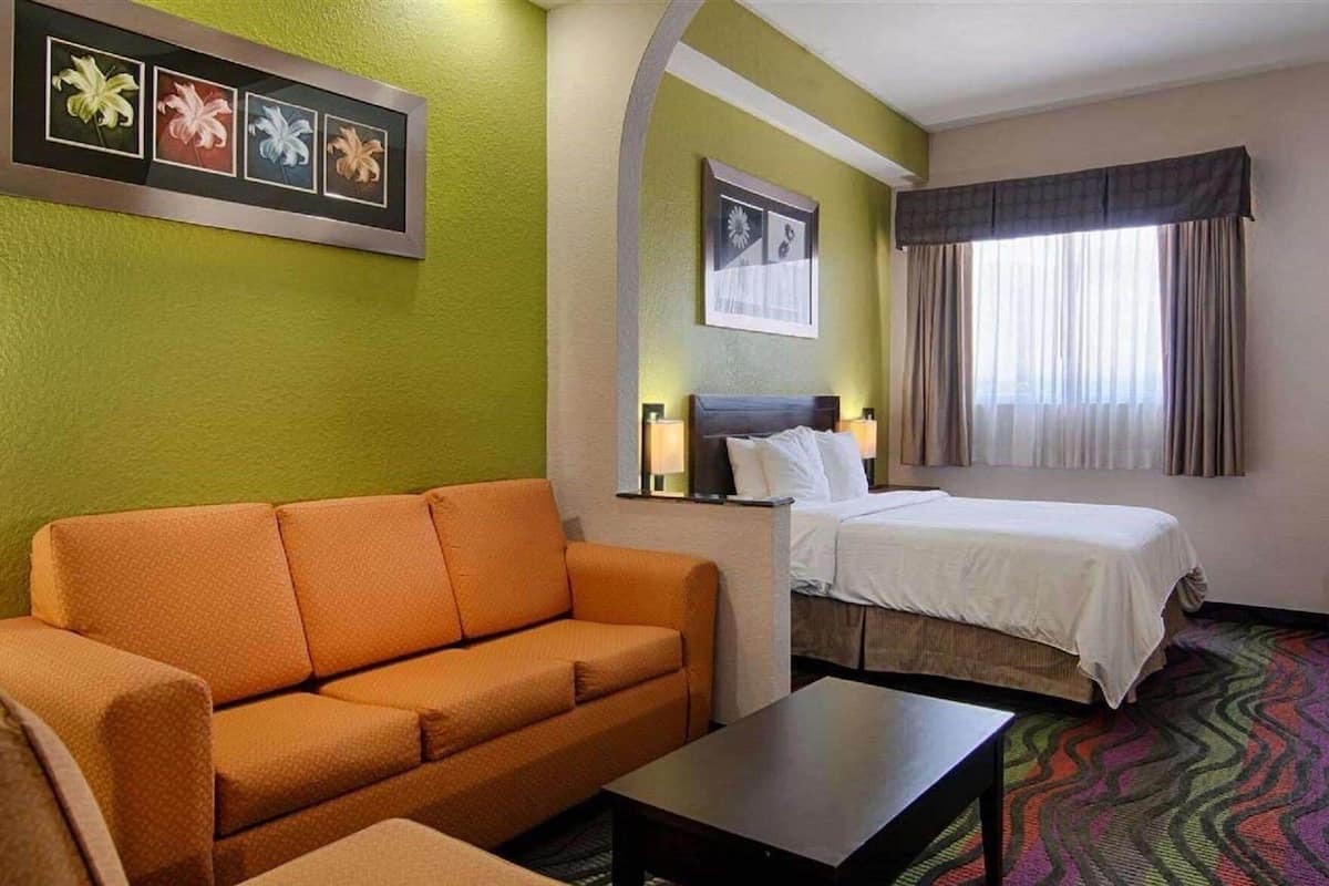 Ein Hotelzimmer mit Sofa, Bett, kleinem Tisch, Nachttisch und einem Fenster mit Vorhängen.