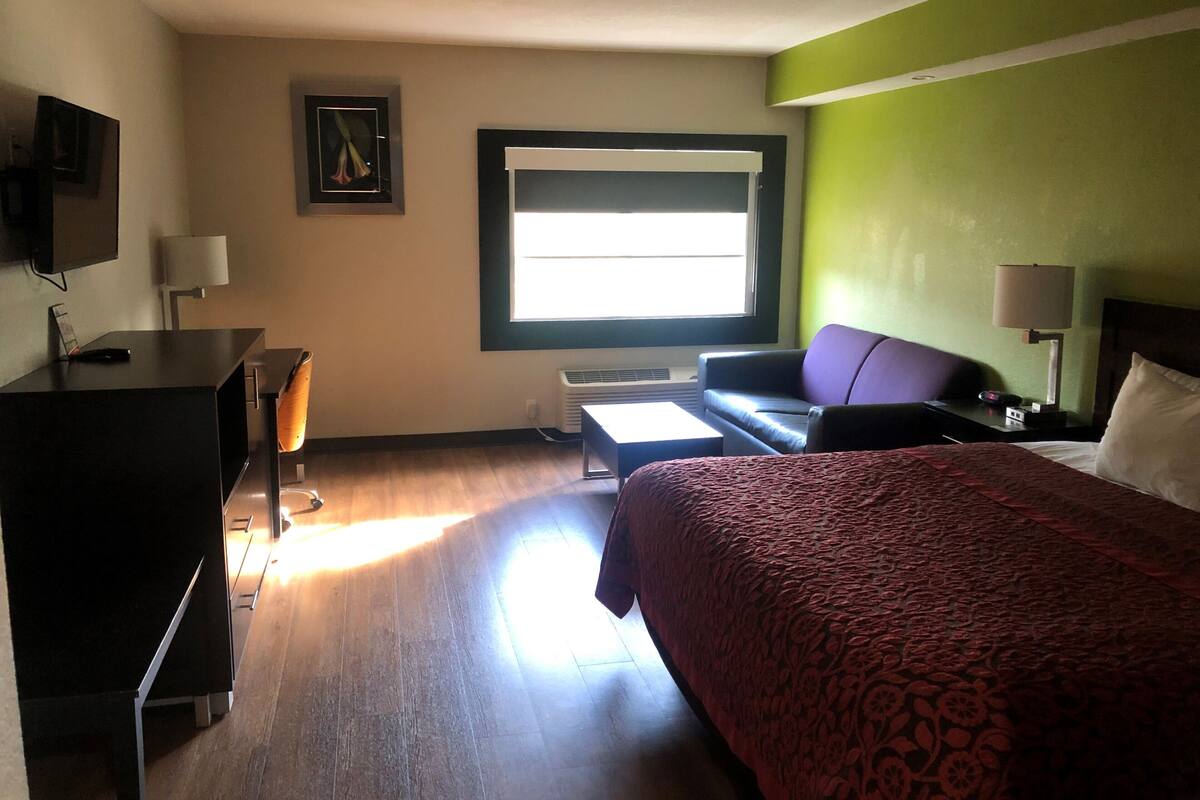 Ein Hotelzimmer mit Bett, Schreibtisch, Stuhl, Fernseher, Fenster und Lampe.