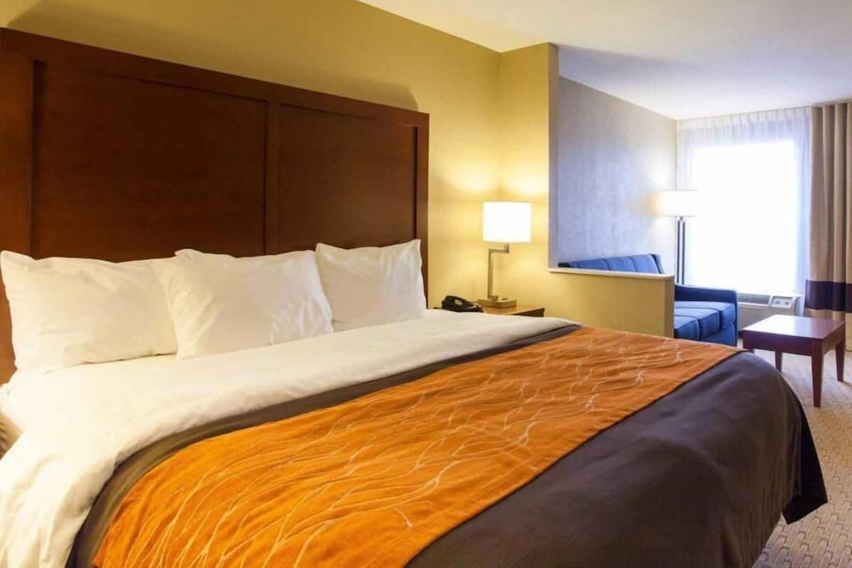 Una habitación de hotel con una cama grande, una mesita de noche con lámpara, una mesita pequeña y una silla.