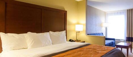 Quarto de hotel com uma cama grande, uma mesinha de cabeceira, uma luminária, uma cadeira e vista para o exterior.