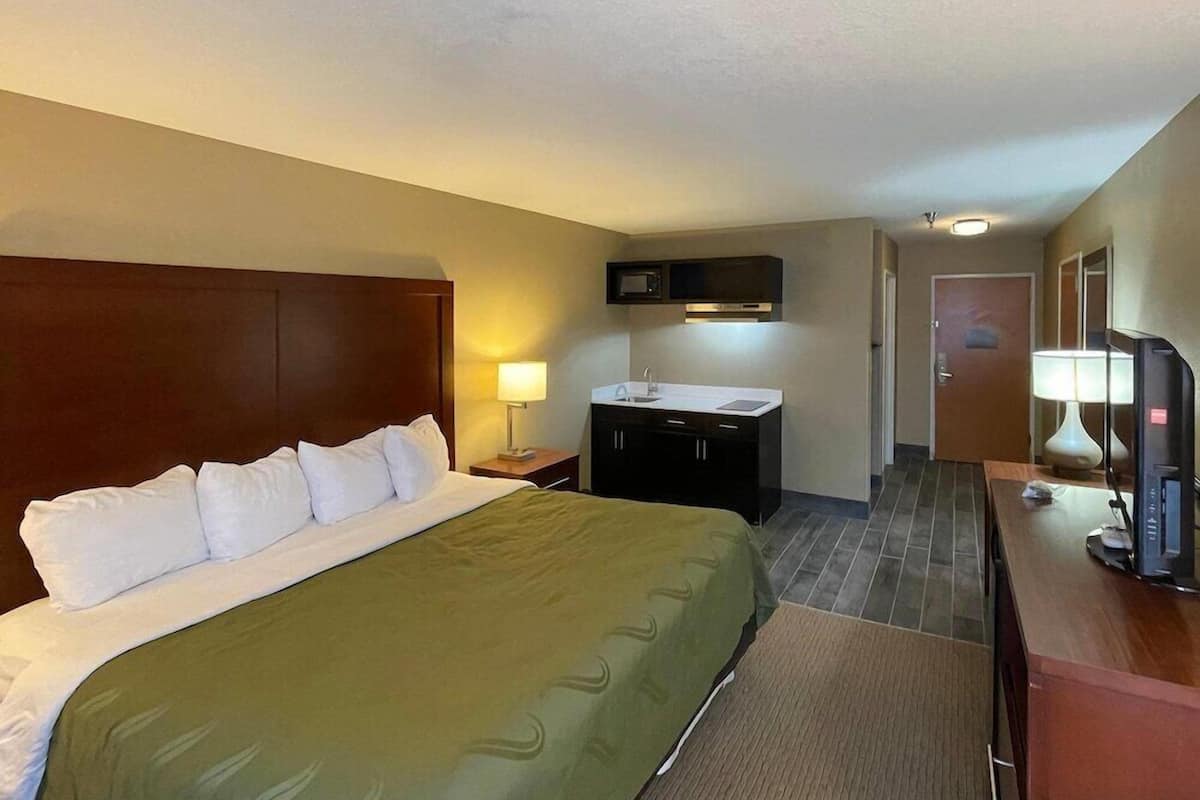 Habitación de hotel con cama, escritorio con computadora, televisor, microondas y puerta de baño.