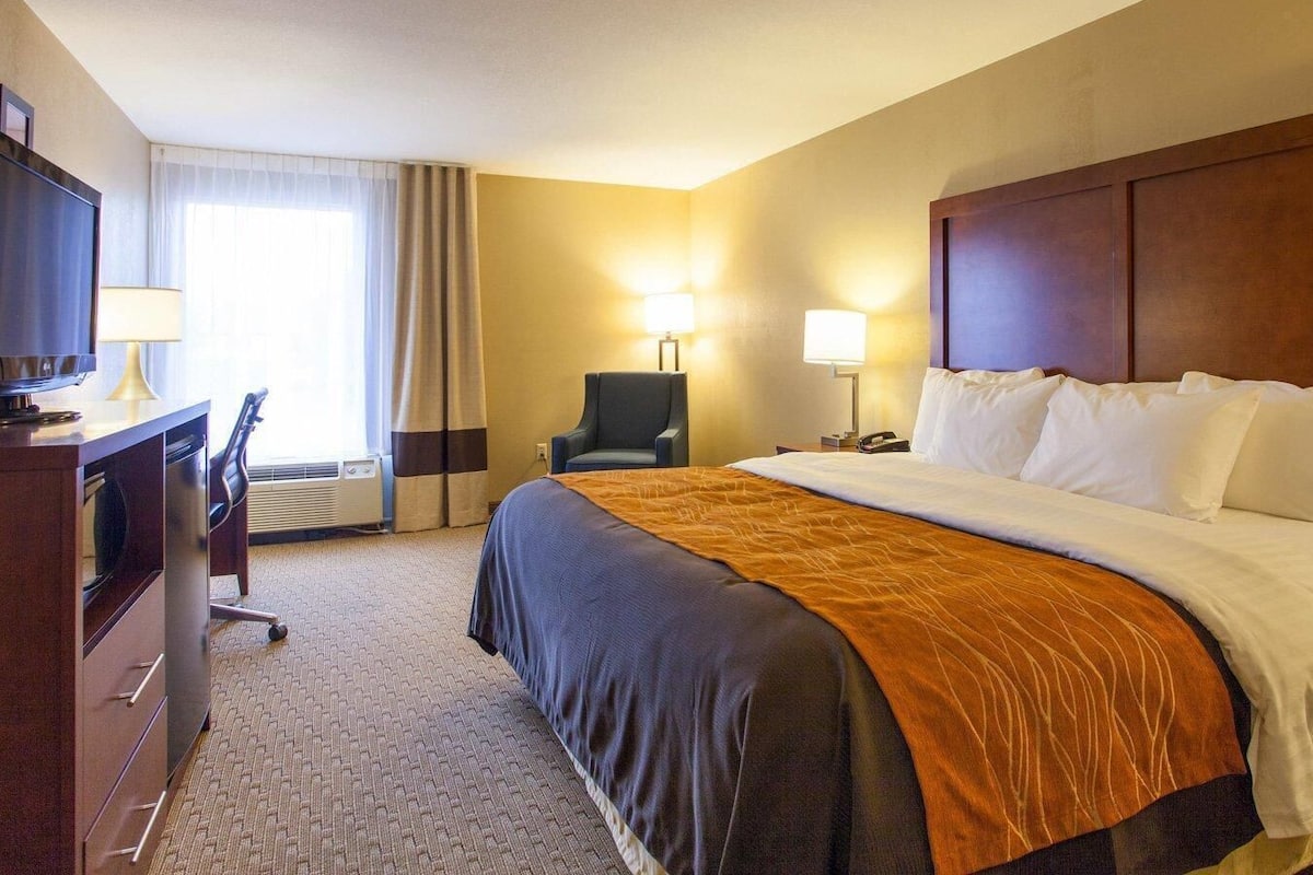 Una habitación de hotel con una cama, un escritorio con silla, un televisor y dos lámparas.