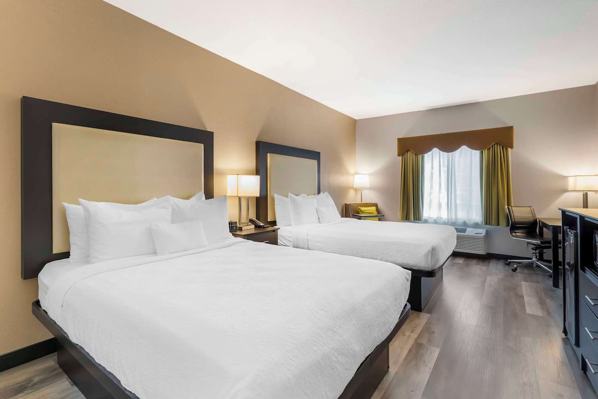 A hotel room with two beds, a desk, a chair, and a window with curtains.
