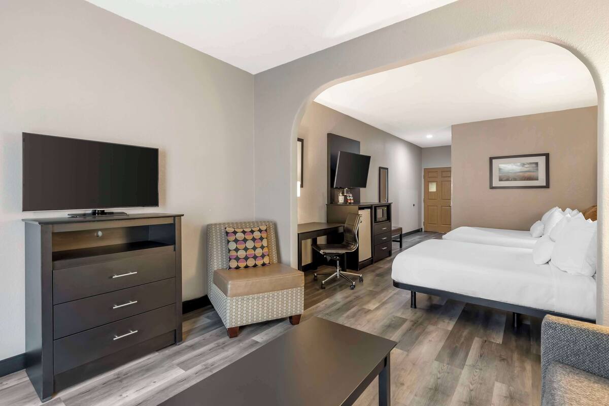 A hotel room with a bed, a desk, a chair, a TV, and a dresser.