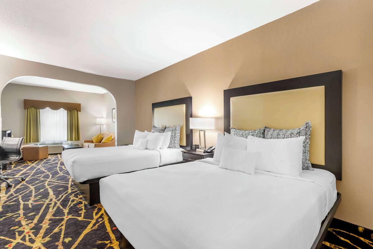 A hotel room with two beds, a desk, a chair, and a large mirror.