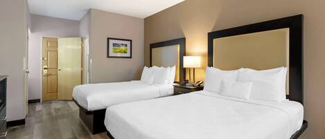A hotel room with two beds, a desk, a chair, a lamp, and a door.