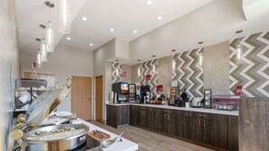A modern kitchen with a buffet setup, including a stove, serving utensils, and a refrigerator. - Best Western Plus Des Moines West Inn & Suites (Clive)