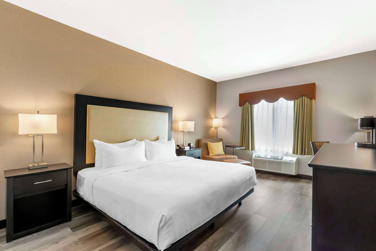 A hotel room with a large bed, bedside tables with lamps, a desk, and a window with curtains.