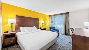 Habitación de hotel con una cama grande, dos mesitas de noche con lámparas, un escritorio, una silla y una ventana con cortinas.