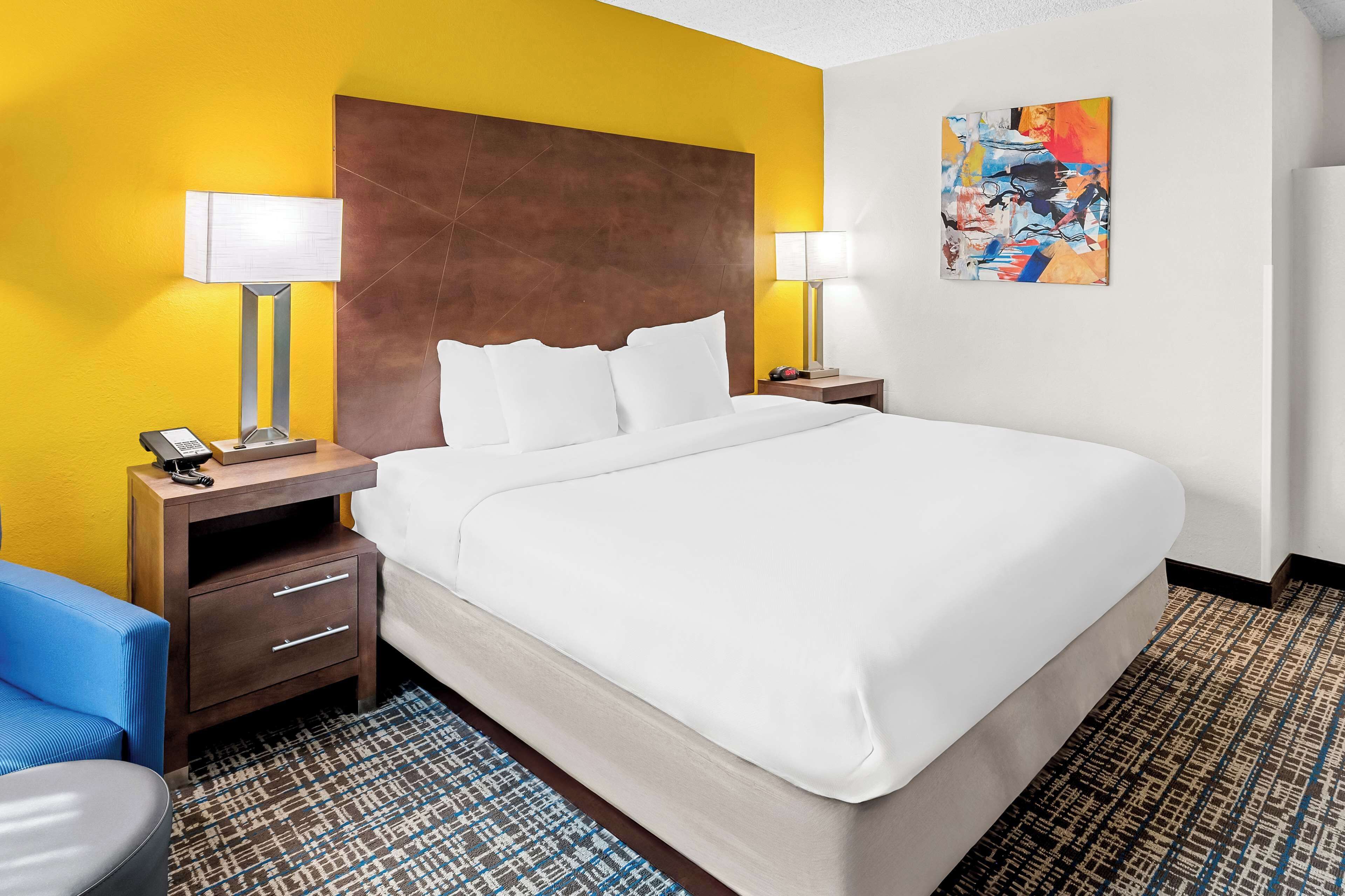 A hotel room with a large bed, two bedside tables with lamps, a blue chair, and a patterned rug.