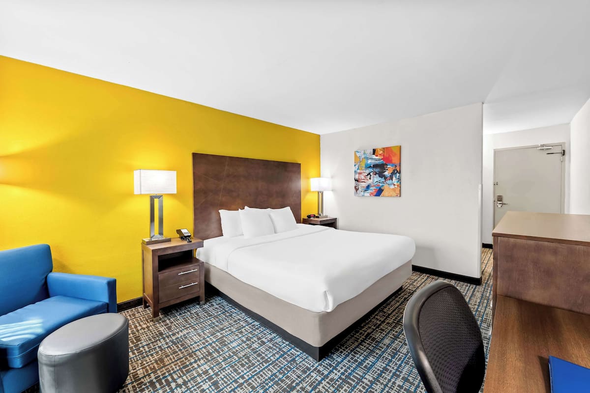 A hotel room with a large bed, a desk, a chair, a sofa, a lamp, and a painting on the wall.