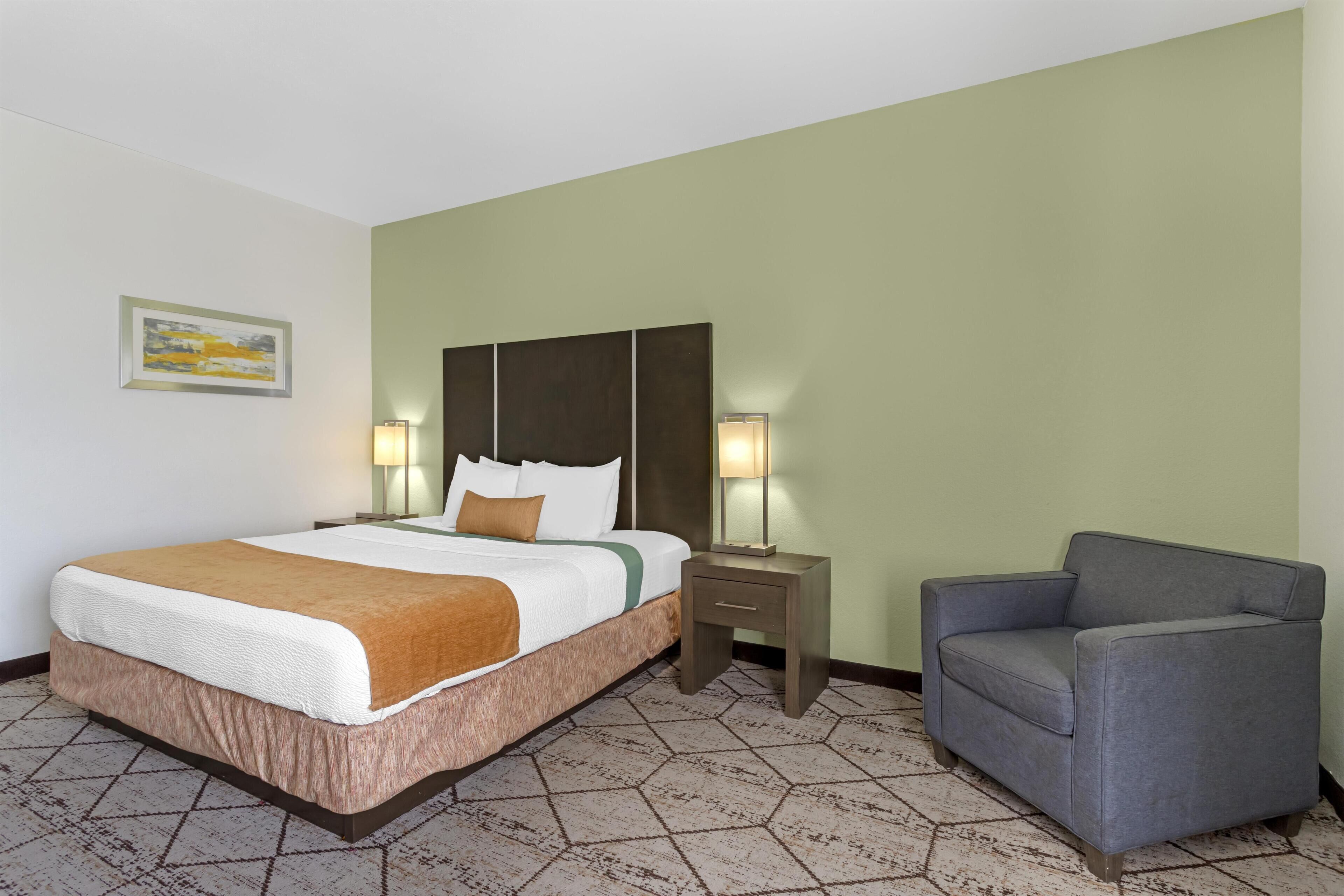 A hotel room with a bed, bedside tables, a chair, and a wall-mounted artwork.
