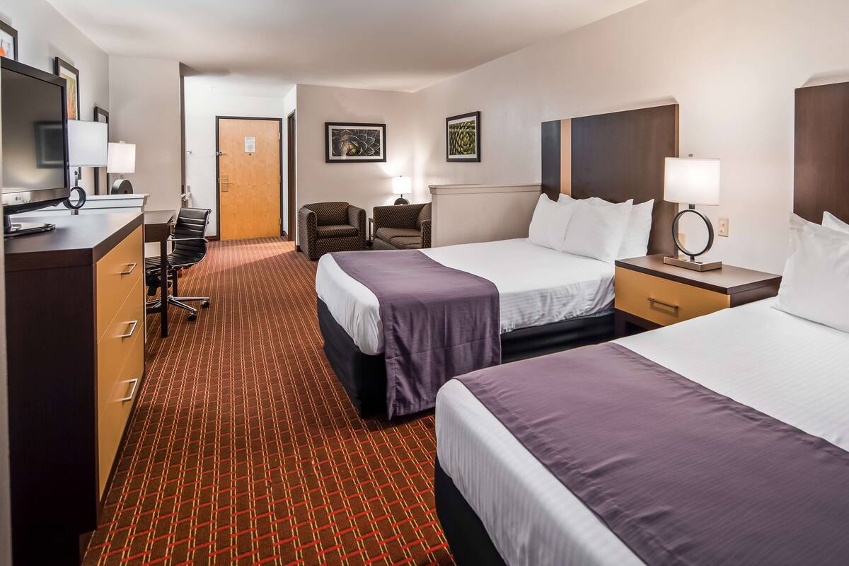 A hotel room with two beds, a desk with a computer, a chair, a TV, and artwork on the walls.