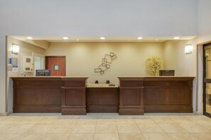 A reception area with a wooden reception desk, a wall-mounted decorative piece, and a potted plant. - Best Western Champions Forest Inn and Suites (Houston)
